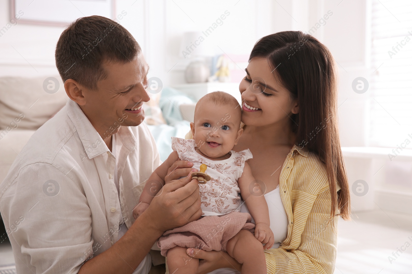 Photo of Happy couple holding their cute little baby with pacifier at home