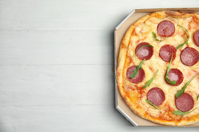 Photo of Tasty pepperoni pizza in cardboard box on white wooden table, top view. Space for text