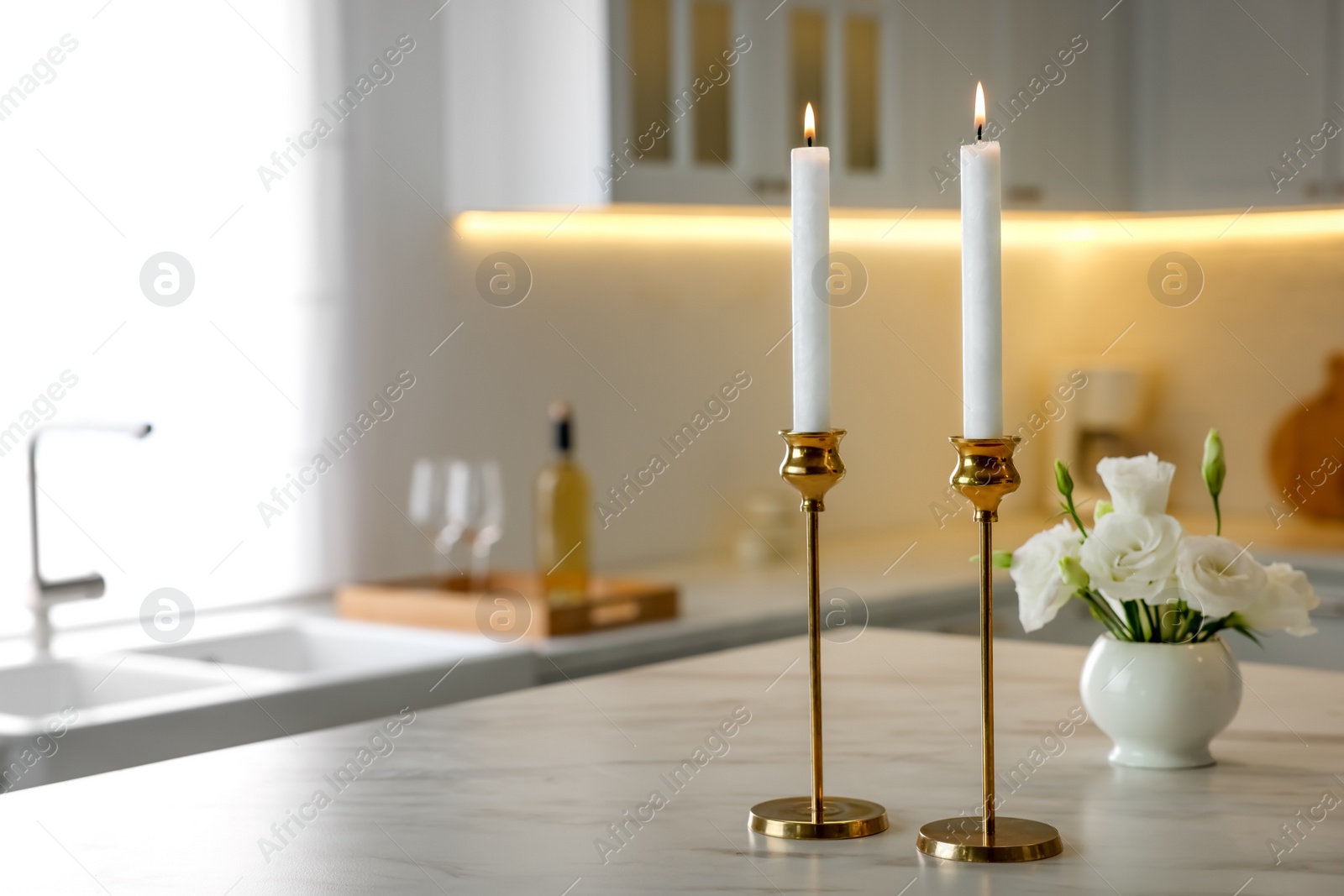 Photo of Pair of beautiful golden candlesticks on white marble table in kitchen, space for text
