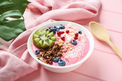 Photo of Tasty smoothie bowl with fresh kiwi fruit, berries and granola on pink wooden table