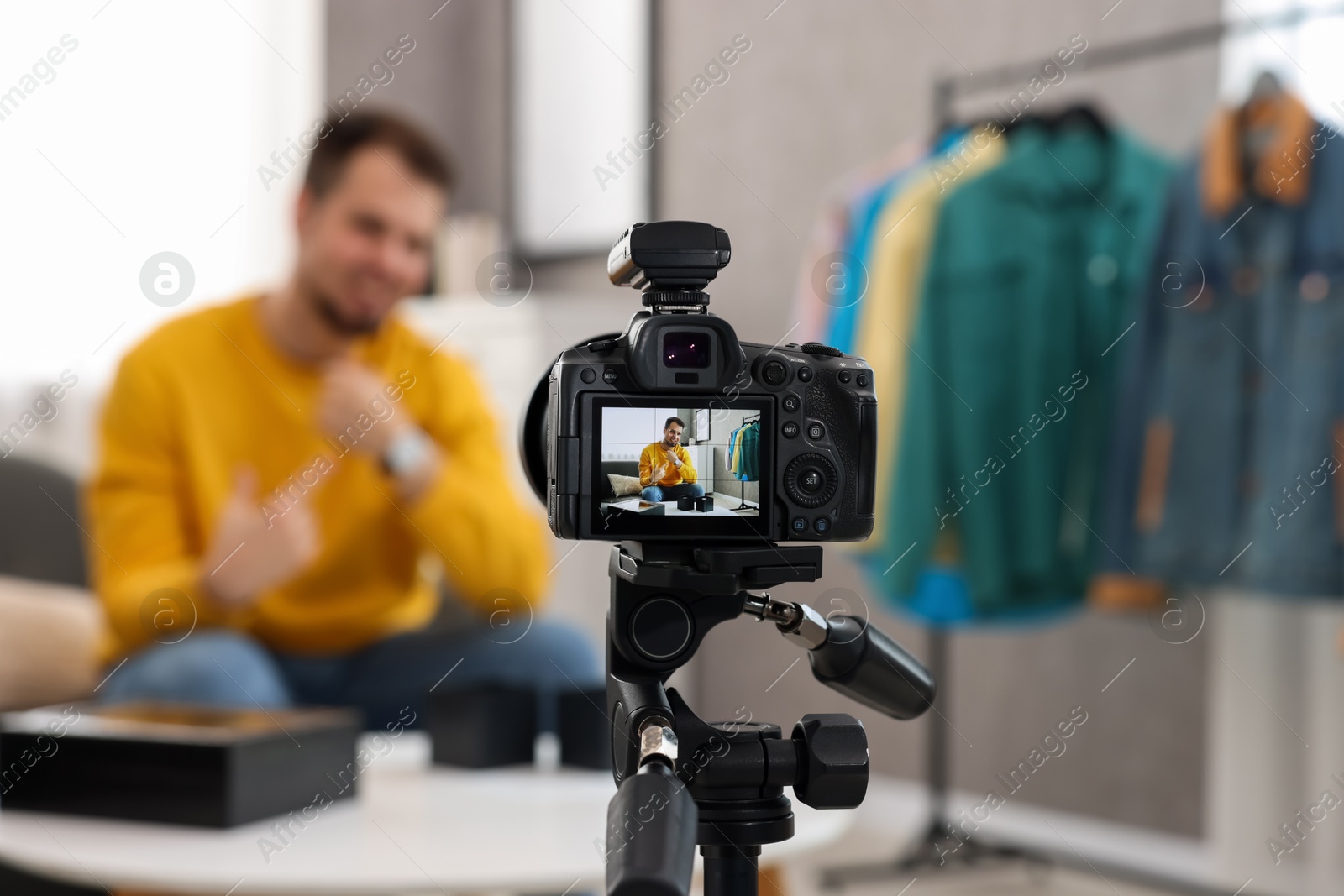 Photo of Fashion blogger showing wristwatch while recording video at home, focus on camera