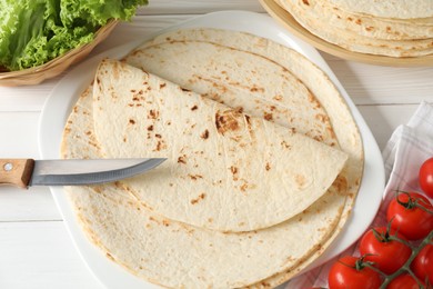 Photo of Tasty homemade tortillas, tomatoes, lettuce and knife on white wooden table, above view