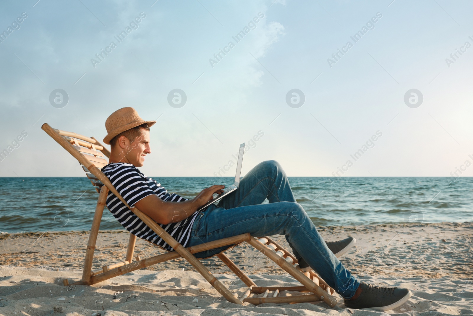 Photo of Man working with laptop in deck chair on beach