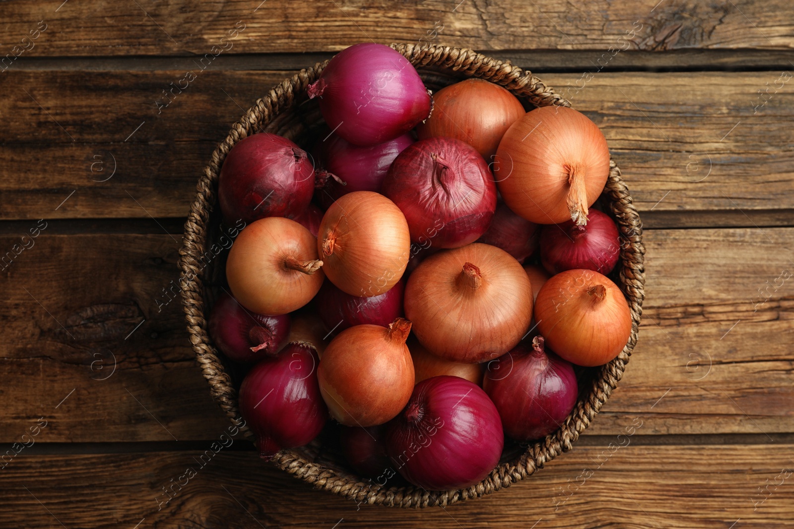 Photo of Onion bulbs in basket on wooden table, top view