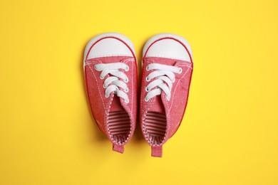 Photo of Cute baby shoes on yellow background, flat lay