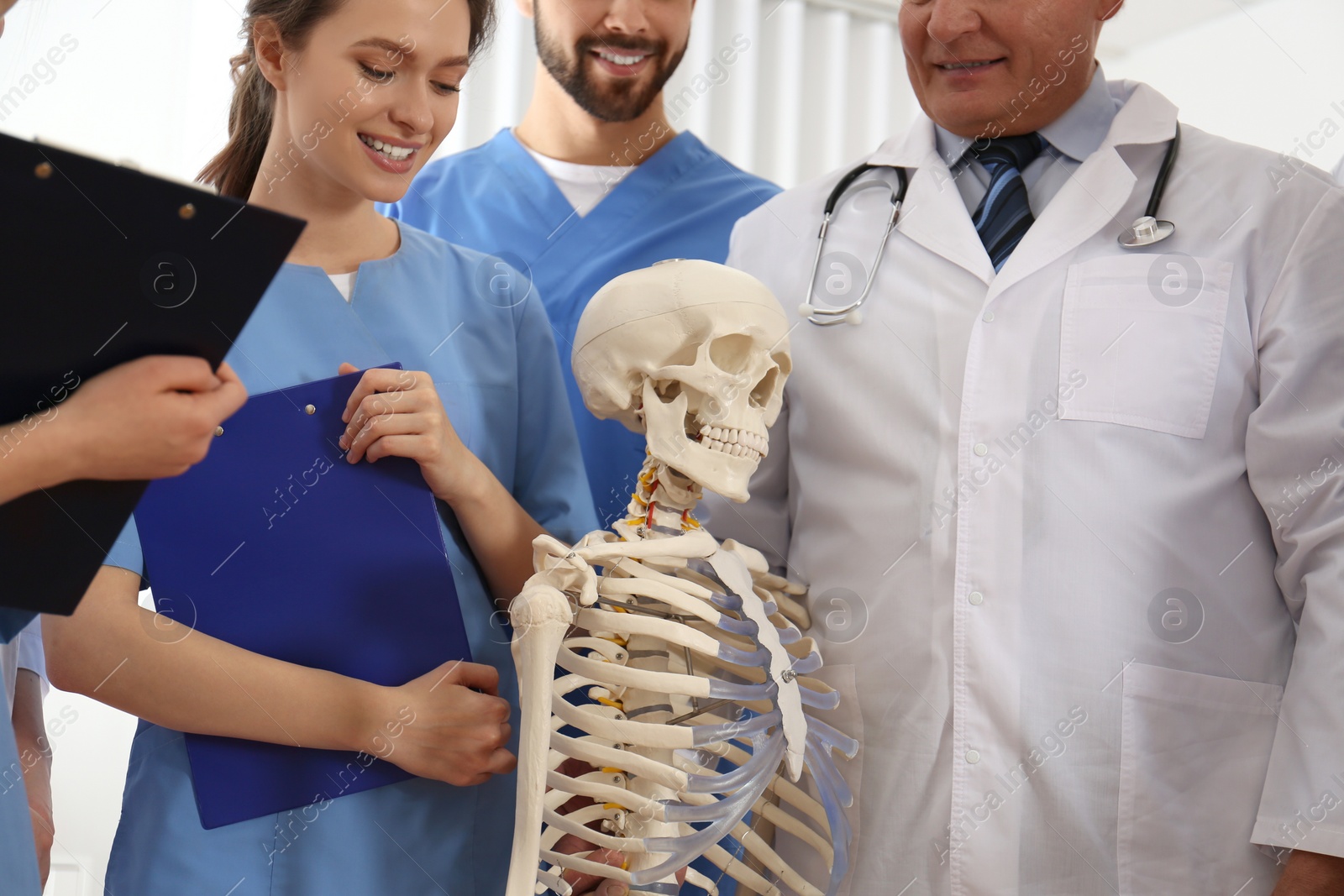 Photo of Professional orthopedist with human skeleton model teaching medical students in clinic