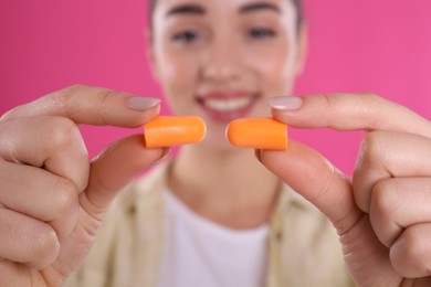 Young woman with foam ear plugs against pink background, focus on hands
