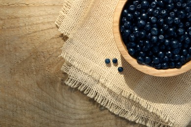 Photo of Bowl of delicious bilberries on wooden table, top view. Space for text