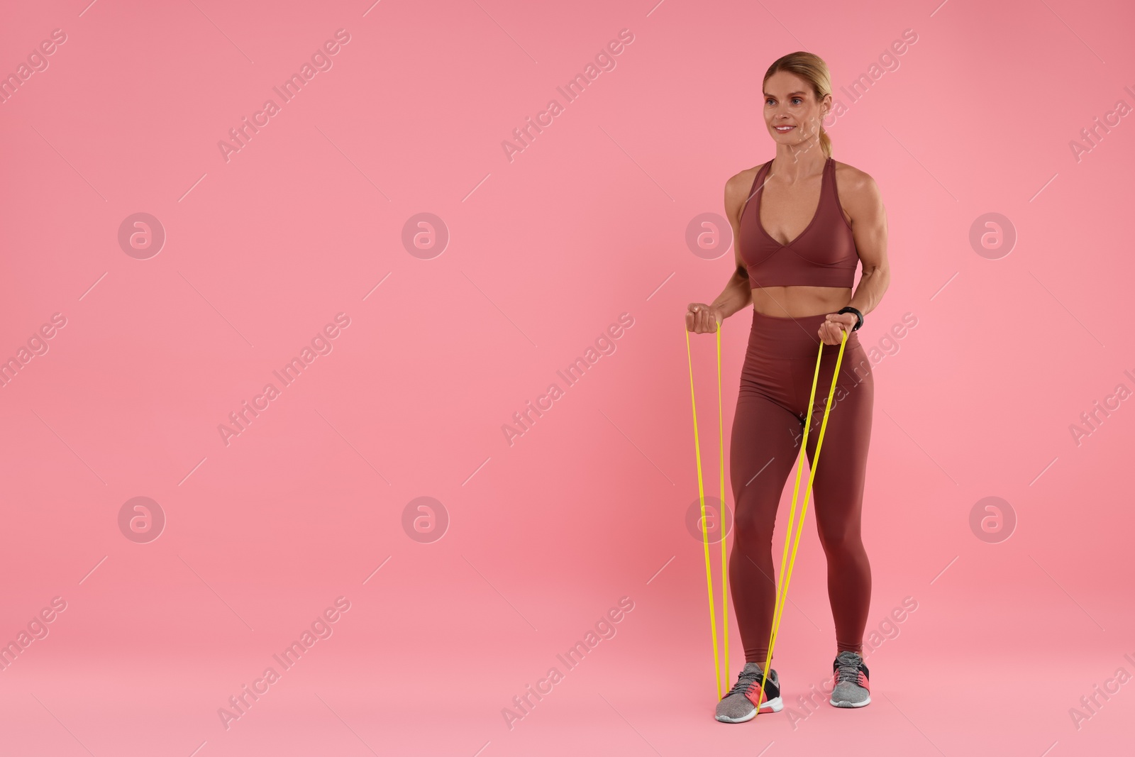 Photo of Woman exercising with elastic resistance band on pink background. Space for text