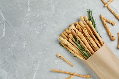 Photo of Delicious grissini sticks and rosemary on grey marble table, flat lay. Space for text
