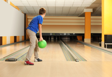 Preteen boy throwing ball at bowling club. Space for text