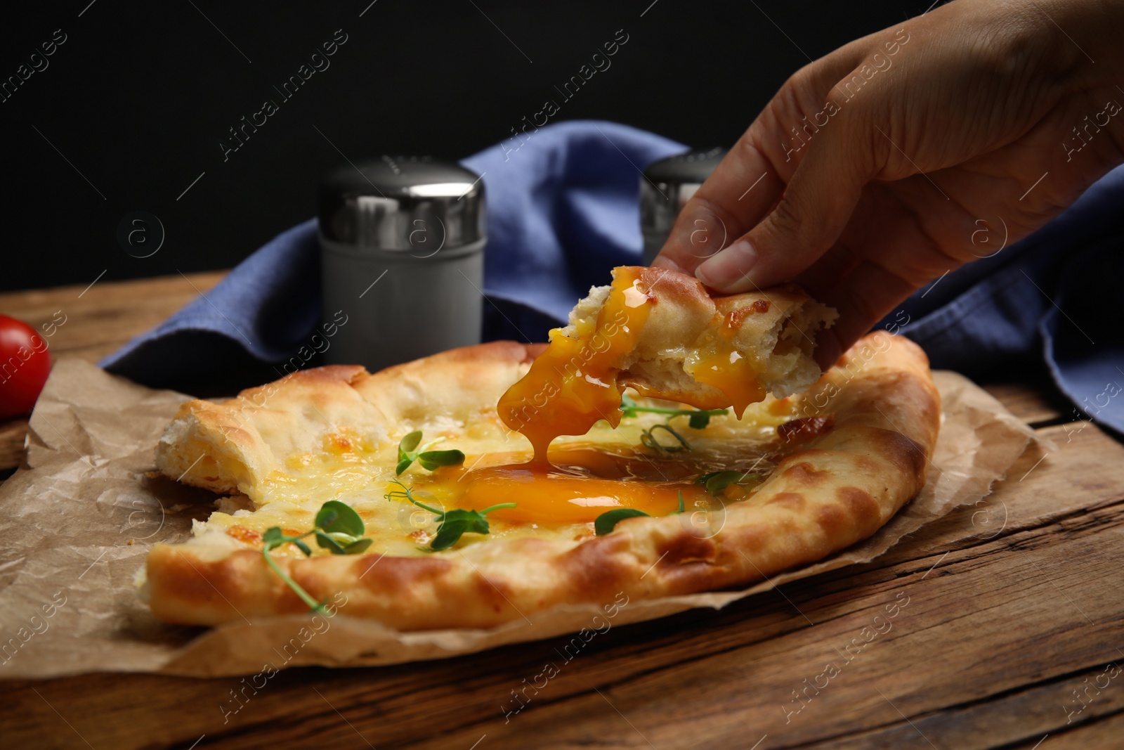 Photo of Woman eating delicious Adjarian khachapuri at wooden table, closeup