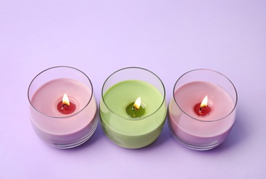 Photo of Burning wax candles in glass holders on purple background