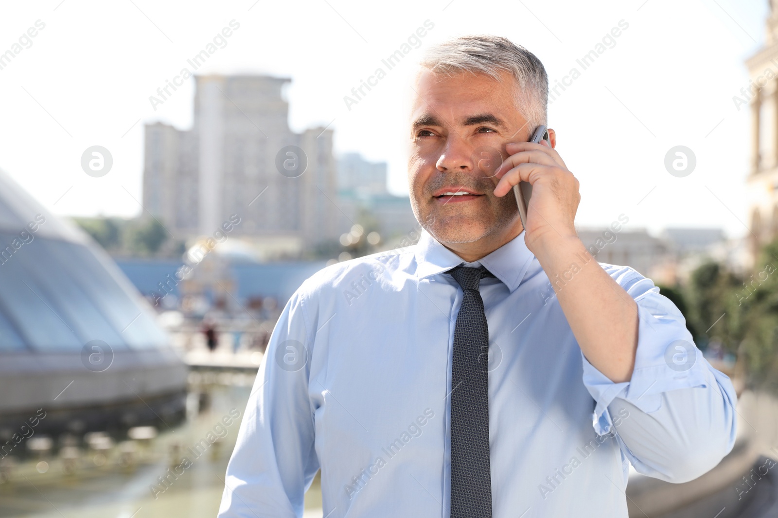 Photo of Handsome businessman talking by mobile phone in city, space for text