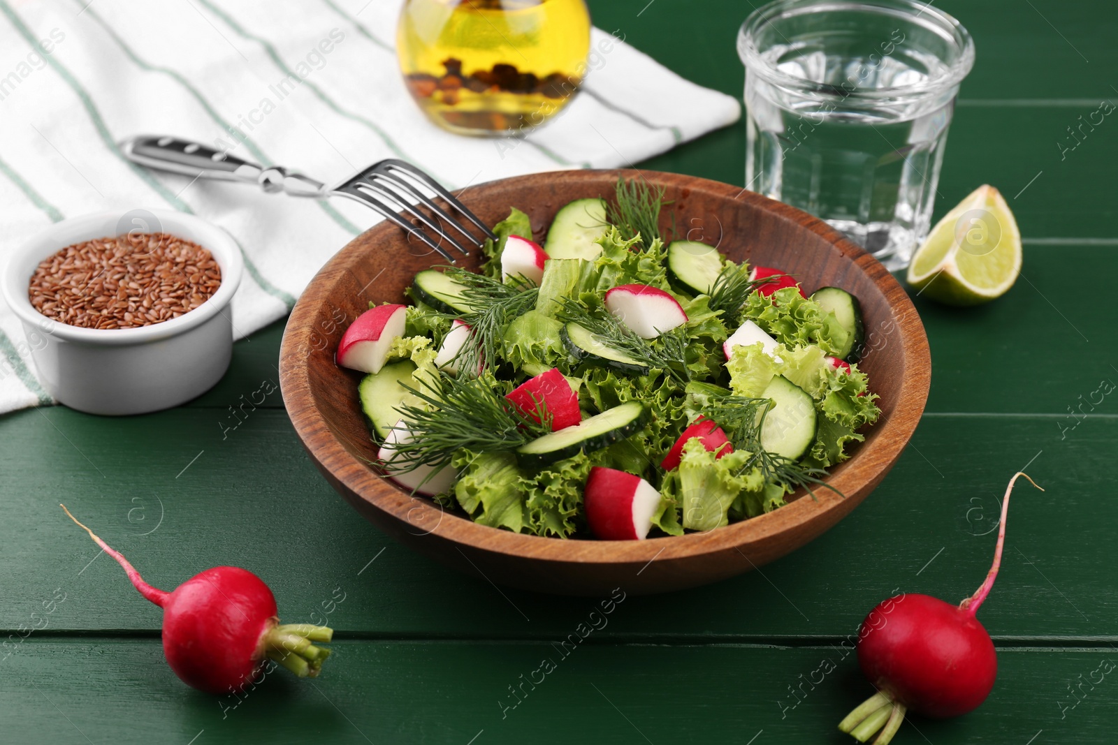 Photo of Delicious salad with radish, lettuce, dill and cucumber served on green wooden table