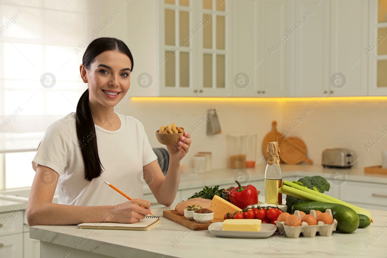 Photo of Happy woman writing in notebook near products at table. Keto diet