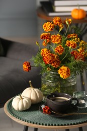Beautiful autumn flowers, cup of coffee and pumpkins on side table indoors
