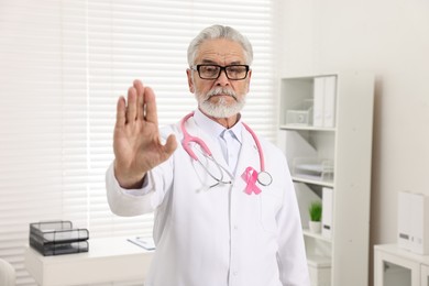 Photo of Mammologist with pink ribbon showing stop gesture in hospital. Breast cancer awareness