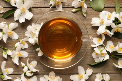 Glass cup of aromatic jasmine tea and fresh flowers on wooden table, flat lay