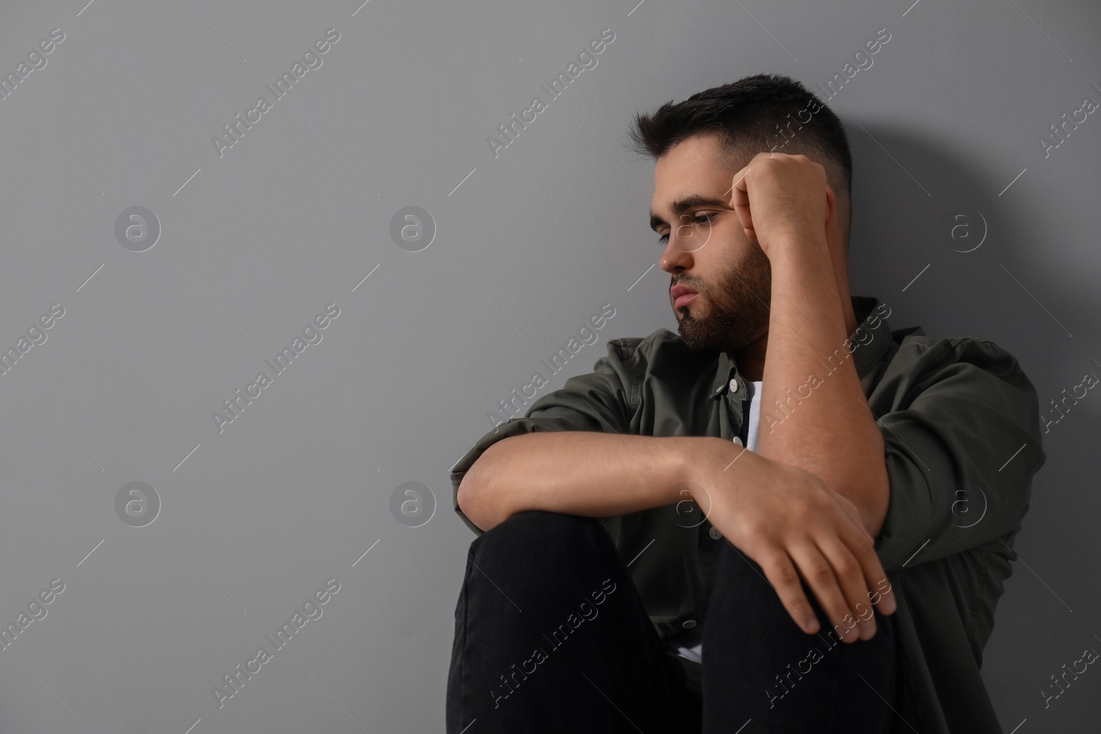 Photo of Sad man sitting near light grey wall. Space for text