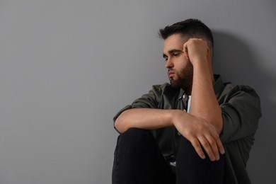 Sad man sitting near light grey wall. Space for text