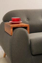 Photo of Cup of tea on sofa with wooden armrest table in room. Interior element