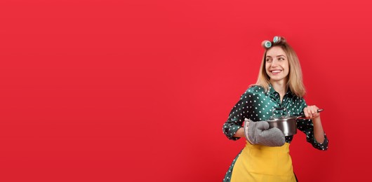 Photo of Young housewife with saucepan on red background. Space for text