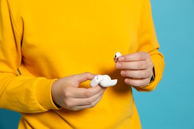 Photo of Man taking out earphones from case on light blue background, closeup