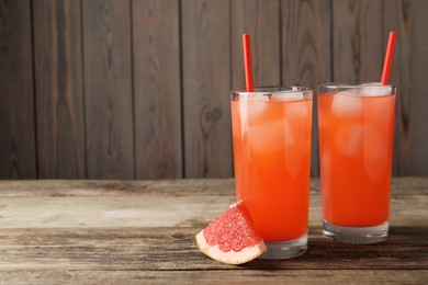 Tasty freshly made grapefruit juice and fruit on wooden table, space for text