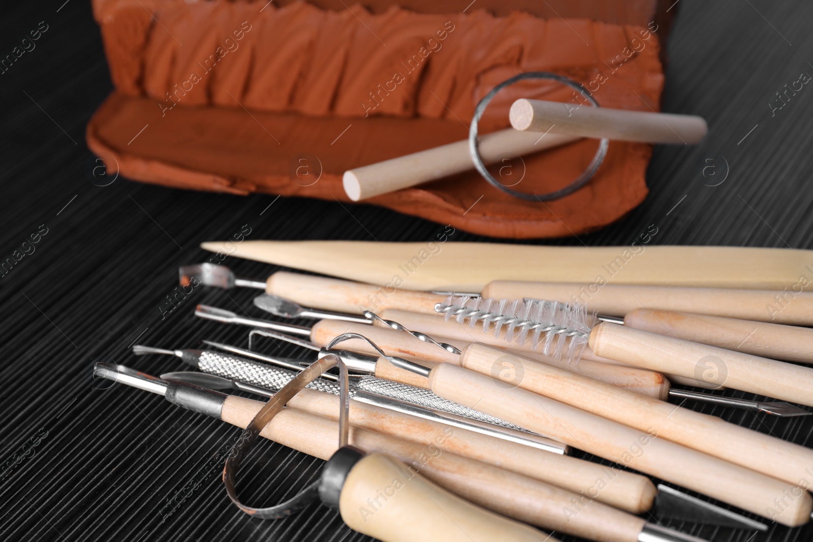 Photo of Clay and set of modeling tools on dark gray wooden table, closeup