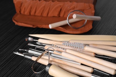 Photo of Clay and set of modeling tools on dark gray wooden table, closeup