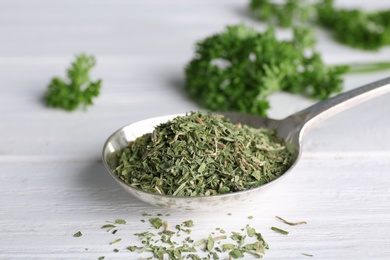 Photo of Spoon with dry parsley on white wooden table