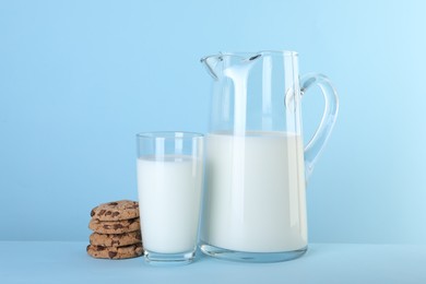 Photo of Jug of fresh milk, glass and cookies on light blue background