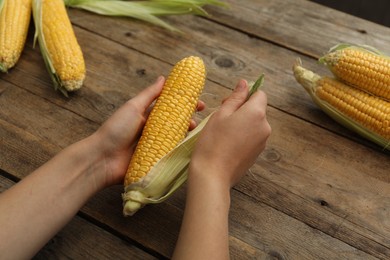 Photo of Woman husking corn cob at wooden table, closeup