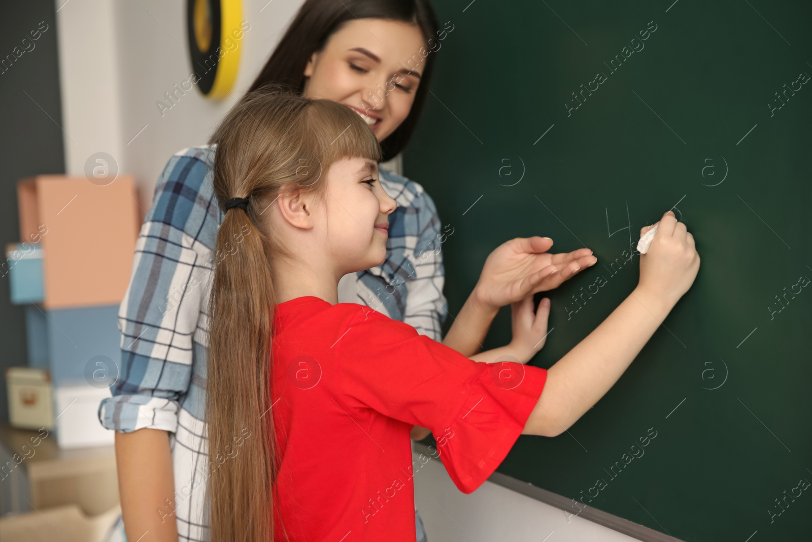 Photo of Young teacher and girl near chalkboard in classroom