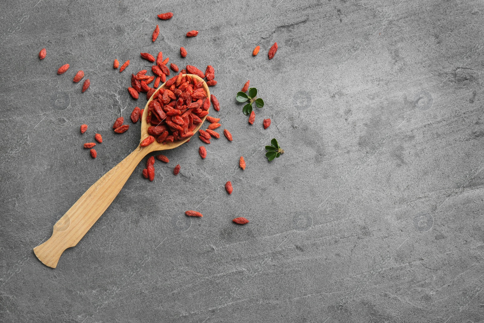 Photo of Spoon and dried goji berries on grey table, top view with space for text. Healthy superfood