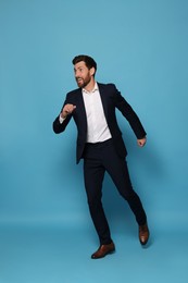 Handsome bearded man in suit running on light blue background