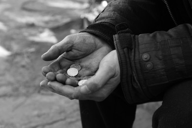 Photo of Poor homeless man holding coins outdoors, closeup. Black and white effect