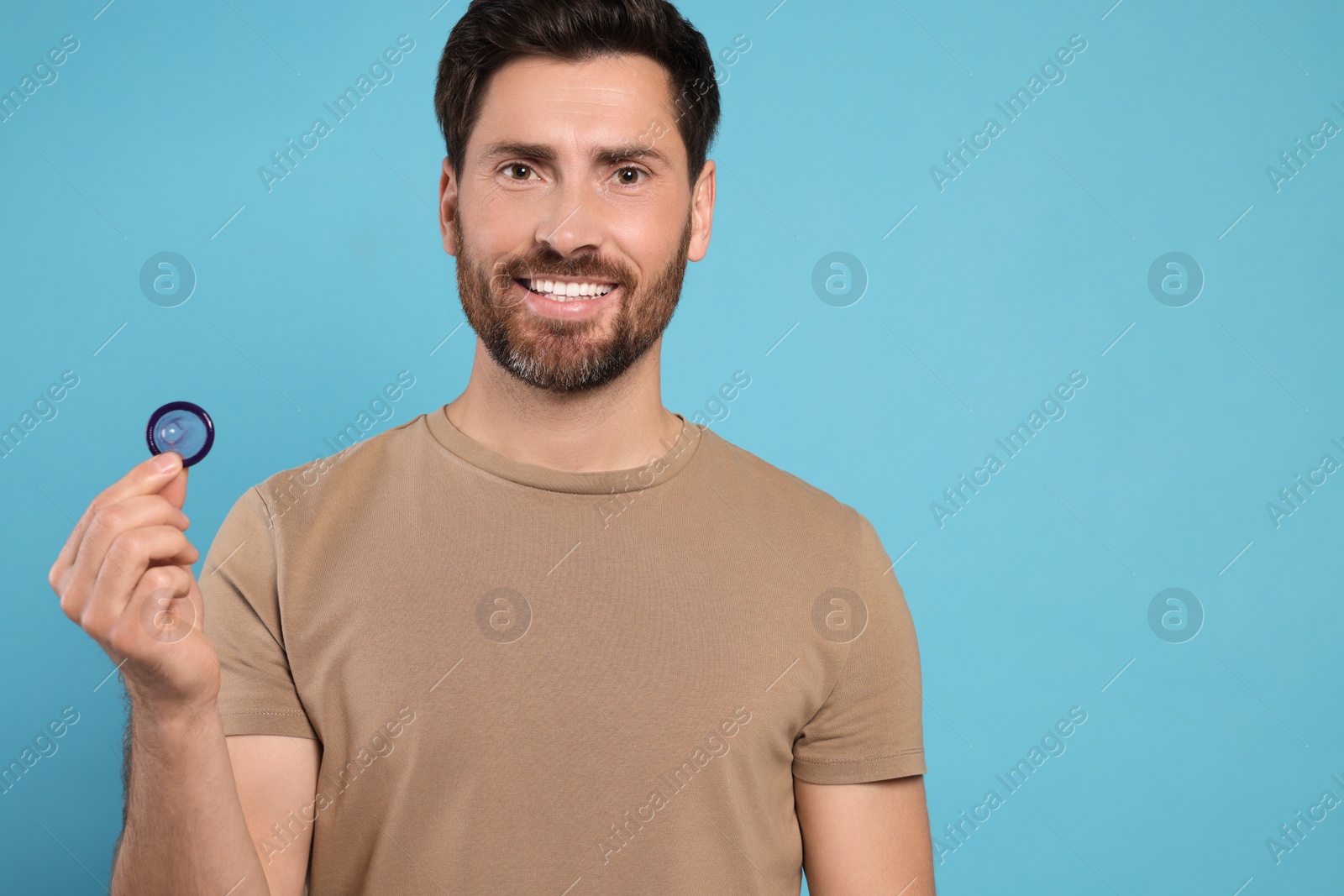 Photo of Happy man holding condom on light blue background, space for text. Safe sex