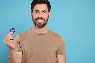 Happy man holding condom on light blue background, space for text. Safe sex