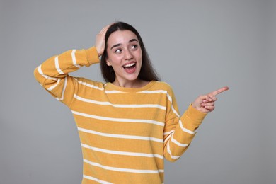 Photo of Portrait of happy surprised woman pointing at something on grey background