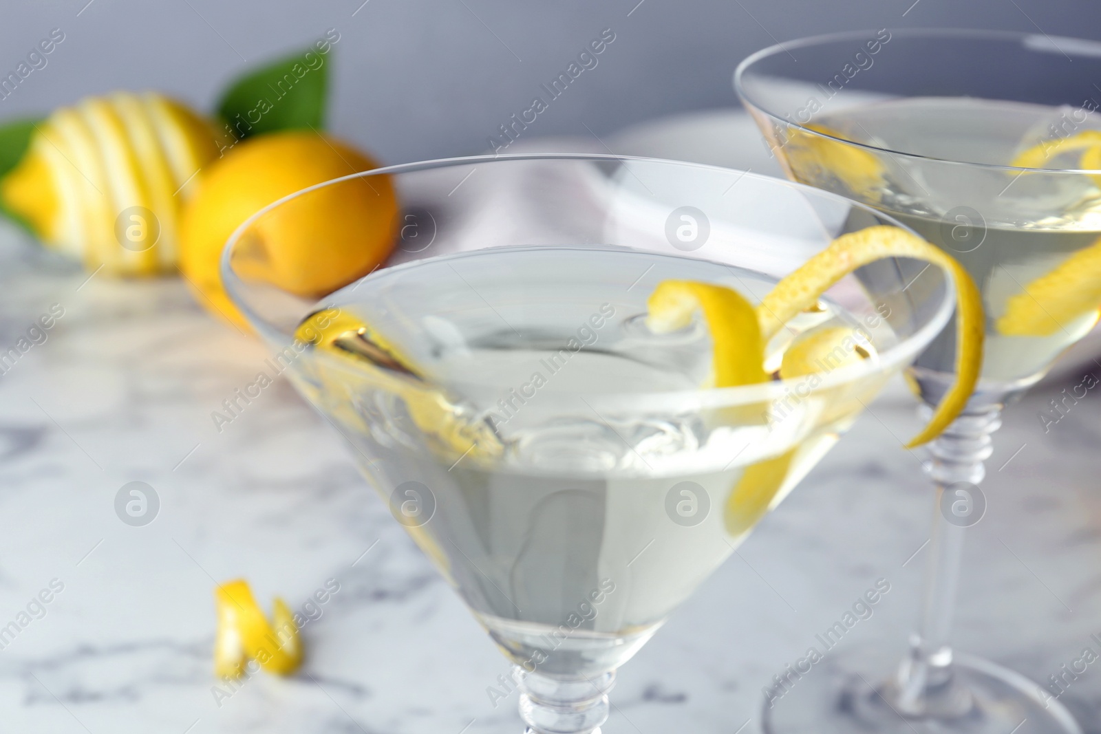 Photo of Glasses of lemon drop martini cocktail with zest on marble table, closeup