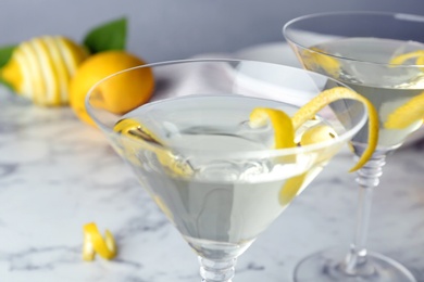 Photo of Glasses of lemon drop martini cocktail with zest on marble table, closeup