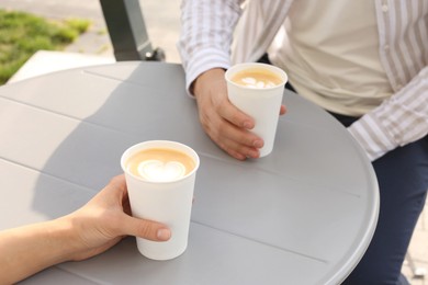 Coffee to go. Couple with paper cups at grey table outdoors, closeup