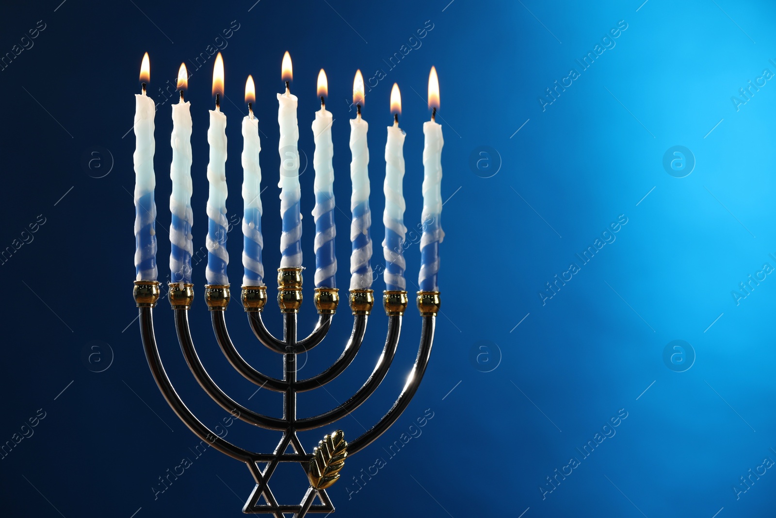 Photo of Hanukkah celebration. Menorah with burning candles on blue background, space for text