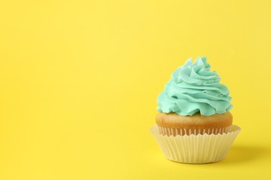 Tasty cupcake with cream on yellow background, space for text