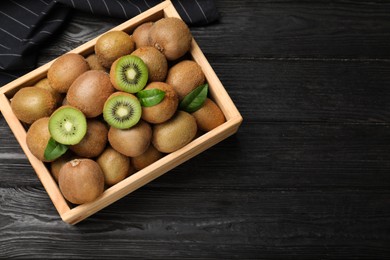 Photo of Crate with cut and whole fresh kiwis on black wooden table, top view. Space for text
