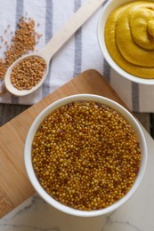 Photo of Bowls and spoon of whole grain mustard on wooden table, flat lay