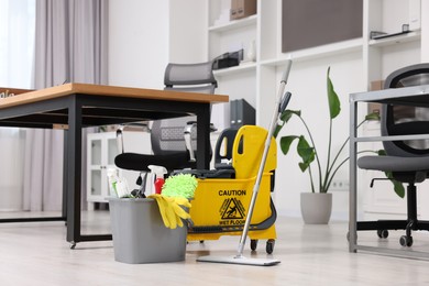 Photo of Cleaning service. Mop, bucket with supplies and wet floor sign in office