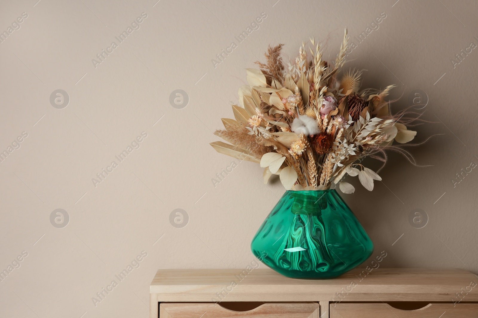 Photo of Beautiful dried flower bouquet in glass vase on wooden table near light grey wall. Space for text